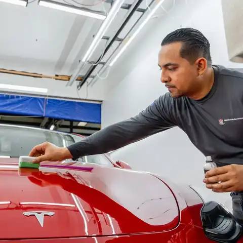 Elvin Sosa, APS Lead Detailer, polishing a red Tesla in our Fairfax shop